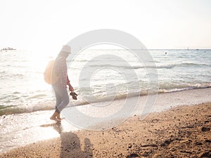 Girl wearing Blue jeans and red plaid shirt and backpacking yellow doing walking on the sea