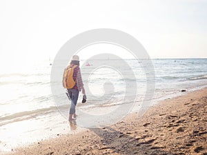 Girl wearing Blue jeans and red plaid shirt and backpacking yellow doing walking on the sea