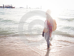 Girl wearing Blue jeans and red plaid shirt and backpacking yellow doing walking on the sea