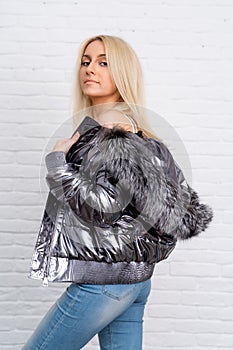 The girl is wearing blue jeans, a white blouse and a gray shiny jacket with a fur hood on a white background.