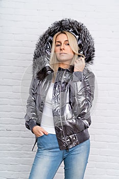 The girl is wearing blue jeans, a white blouse and a gray shiny jacket with a fur hood on a white background.