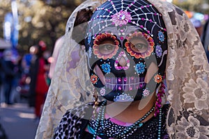 Girl wearing colorful skull mask and lace veil for Dia de Los Muertos/Day of the Dead