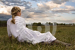 Girl wearing a dress sitting in a pasture