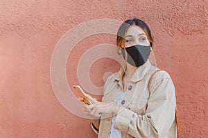 Girl wearing an ecologic and reusable mask  and holding a mobile phone with an orange wall on the background