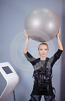 Girl wearing electrical muscular stimulation suit doing exercise with ball.