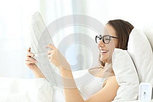 Girl wearing eyeglasses reading a newspaper on the bed