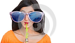 Girl wearing funky blue sunglasses drinking soft drink with straw isolated on white background, funny girl,female model