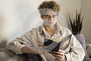 Girl wearing glasses is sitting on the couch and reading a book
