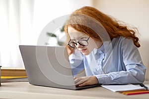 Girl wearing glasses sitting at table, using laptop