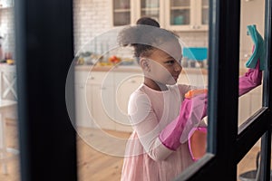 Girl wearing gloves cleaning the glass door helping her mom