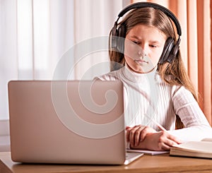 Girl wearing headphones using laptop to watch online seminar. E-learning concept. Distance education