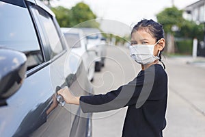 Girl wearing mask is opening car door. Female kids wear face mask during COVID-19 outbreak