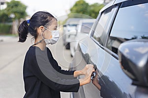 Girl wearing mask is opening car door. Female kids wear face mask during COVID-19 outbreak