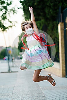 Girl wearing a mask takes a jump for joy at going back to school.