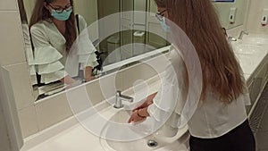 a girl wearing medical mask washes her hands a public toilet