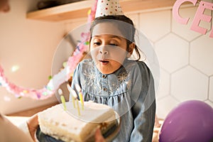 Girl wearing party cap blowing on the candles at her birthday cake