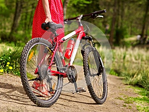 Girl wearing red polka dots dress rides bicycle into park.