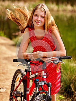 Girl wearing red polka dots dress rides bicycle into park.