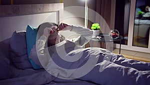 A girl wearing a sleep mask suffers from insomnia while lying in bed at night in her home, evening light