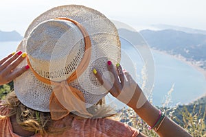 Girl wearing straw hat looking at the seaside from mountain view