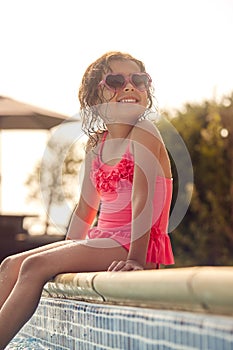 Girl Wearing Sunglasses Having Fun Sitting On Edge Of Swimming Pool On Summer Vacation