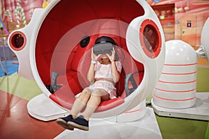 Girl wearing virtual reality googles and experiencing virtual reality in moving interactive chair at amusement park