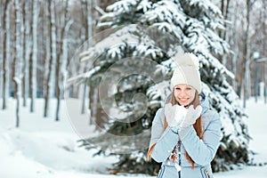 A Girl Wearing Warm Winter Clothes And Hat Blowing Snow In Winter Forest, horizontal. Model with a beautiful smile near the Christ