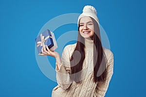 Girl wearing white oversize sweater and hat, holding present box for christmas