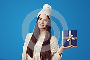 Girl wearing white oversize sweater and hat, holding present box for christmas