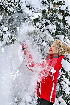 Girl wearing winter clothes shakes off from branches of trees.