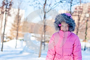 A girl wearing winter warm clothes - down jacket and fur hood enjoying sunny day in the park. Happy child wintertime