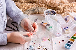 A girl weaves a beaded bracelet on a table among boxes of beads. Ð¡hildren`s hobby