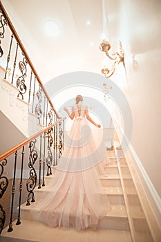 A girl in a wedding dress is walking up the stairs. beige dress. Beautiful lady in luxurious ballroom dress walking up the stairs