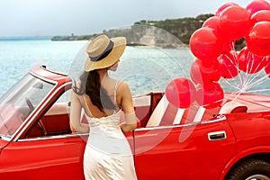 Girl at the wedding in a white dress stands near the red retro car