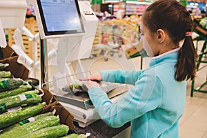 Girl weighs fresh cucumbers on scales at the store