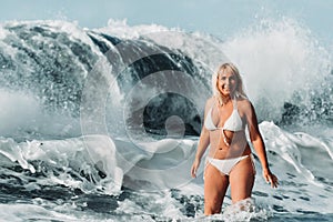 A girl with wet hair jumps over large waves in the Atlantic ocean, around a wave with splashes of spray and water drops.Tenerife.