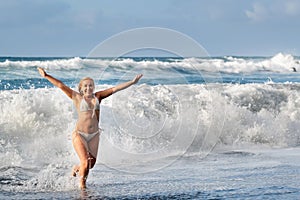 A girl with wet hair jumps over large waves in the Atlantic ocean, around a wave with splashes of spray and water drops.Tenerife.