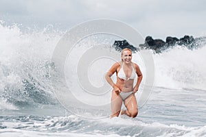 A girl with wet hair jumps over large waves in the Atlantic ocean, around a wave with splashes of spray and water drops.Tenerife.