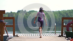 Girl in wetsuit jumping into the lake from wooden pier. Having fun on summer day
