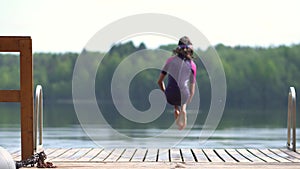 Girl in wetsuit jumping into the lake from wooden pier. Having fun on summer day