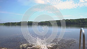 Girl in wetsuit jumping into the lake from wooden pier. Having fun on summer day