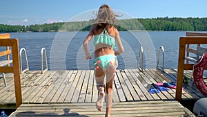 Girl in wetsuit jumping into the lake from wooden pier. Having fun on summer day.