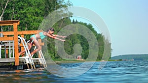 Girl in wetsuit jumping into the lake from wooden pier. Having fun on summer day.