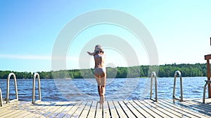 Girl in wetsuit jumping into the lake from wooden pier. Having fun on summer day.