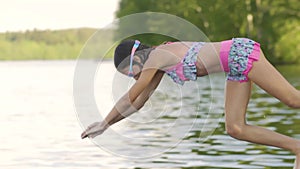 Girl in wetsuit jumping into the lake from wooden pier. Having fun on summer day.
