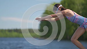 Girl in wetsuit jumping into the lake from wooden pier. Having fun on summer day.