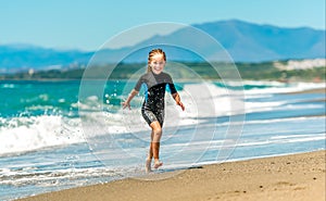 Girl in a wetsuit running along the beach