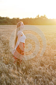 Girl in wheat field standing arms outstretched at sunset and enjoy the outdoors, side view