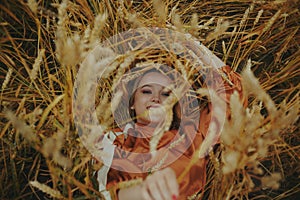 The girl in wheat lies in a dress and laughs. Golden spikelets of millet. Concept of unity with nature