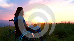 Girl in a wheelchair sits on a sunset background soft focus